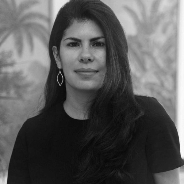 Ana in black in white staring at the camera. She has long dark hair and is wearing a black t shirt