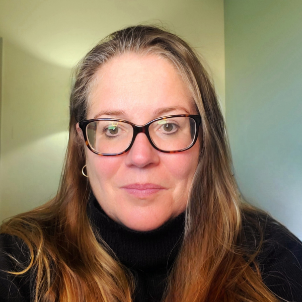 Eliza smiles at the camera. She is wearing glasses and a black shirt