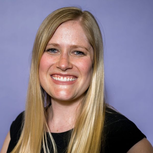 Emily smiling at the camera. She has blonde hair, wearing a black top, and there is a purple background