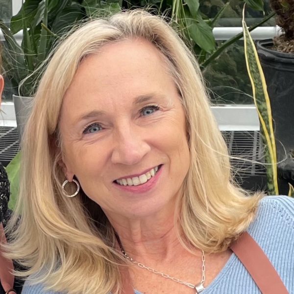 Ingrid smiling at the camera. She has shoulder length blonde hair and is wearing a light blue sweater