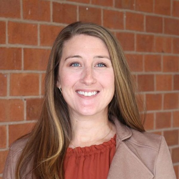 Jacqueline smiling at camera in front of brick background