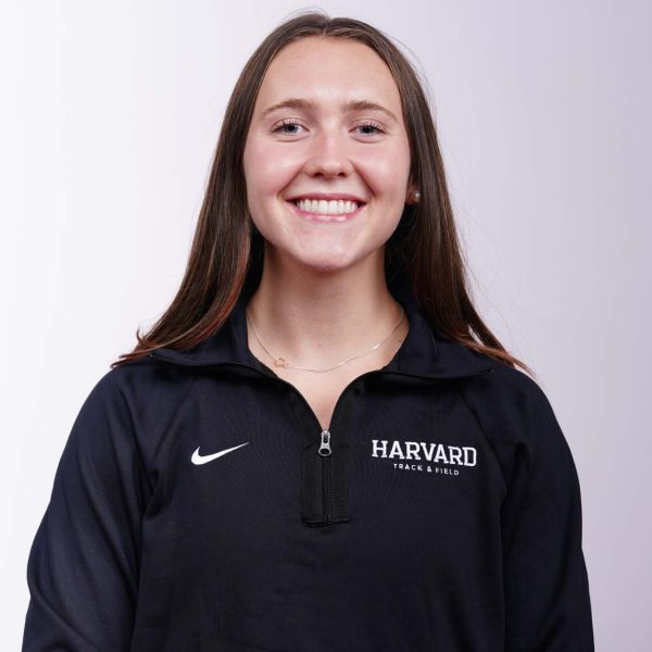 Kaelin is smiling at the camera. She has medium length brown hair and is wearing a black quarter zip Harvard sweater