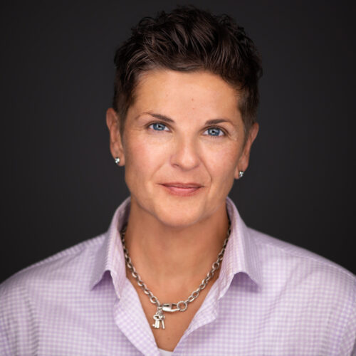 Amy looking at the camera. She has short brown hair and is wearing a pink button up