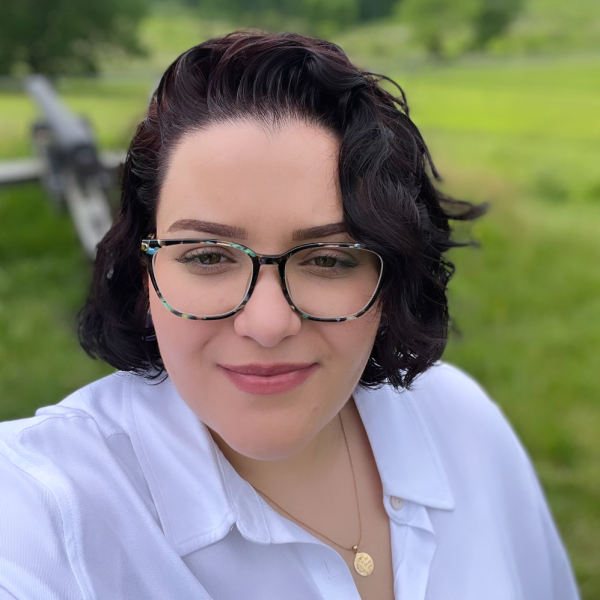 Cas smiling at the camera, wearing a collared white shirt, with greenery in background.