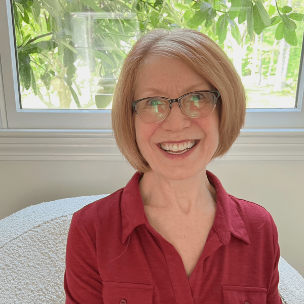 Gayle smiling at the camera, wearing a collared red shirt, with greenery in background