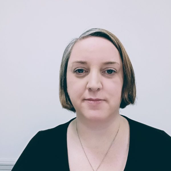 Jill smiling at camera. She's wearing a black shirt against a gray background.