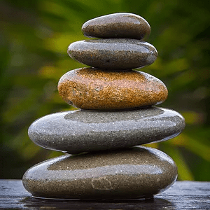 Stack of five smooth stones of varying sizes and colors in a lush green setting.